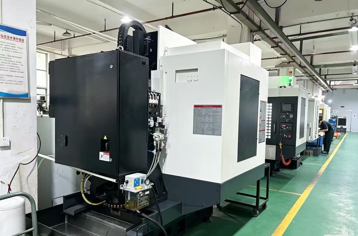 Row of CNC machining centres in a workshop with a worker at the far end